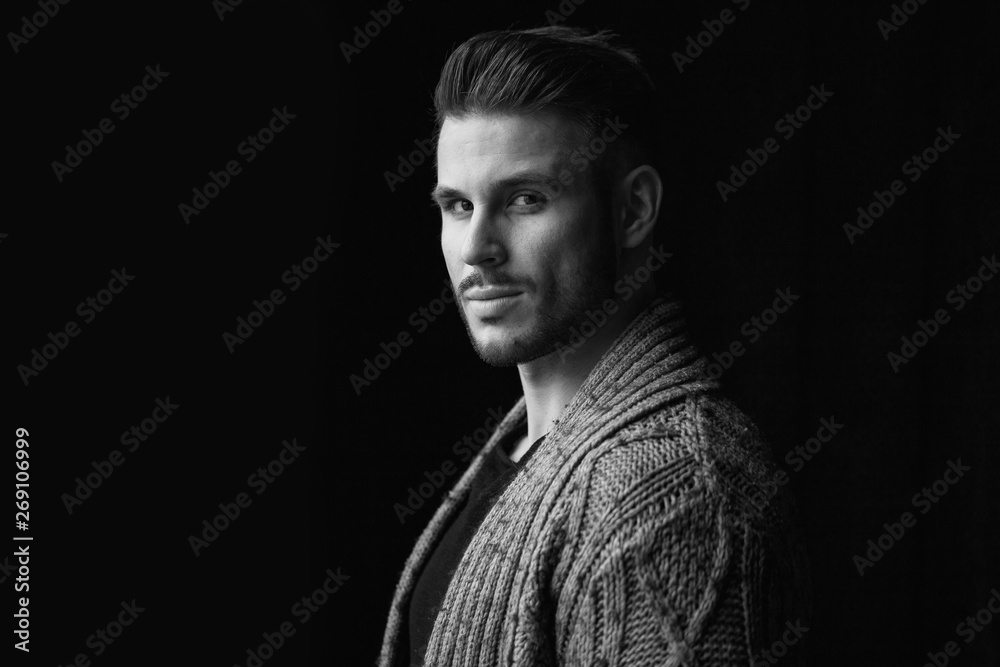 Black and white. Muscular model young man with beard in knitted sweater on dark background. Fashion portrait of brutal sporty sexy strong guy with modern trendy hairstyle. Model, fashion concept. Black and white. Muscular model young man with beard in knitted sweater on dark background. Fashion portrait of brutal sporty sexy strong guy with modern trendy hairstyle. Model, fashion concept.
