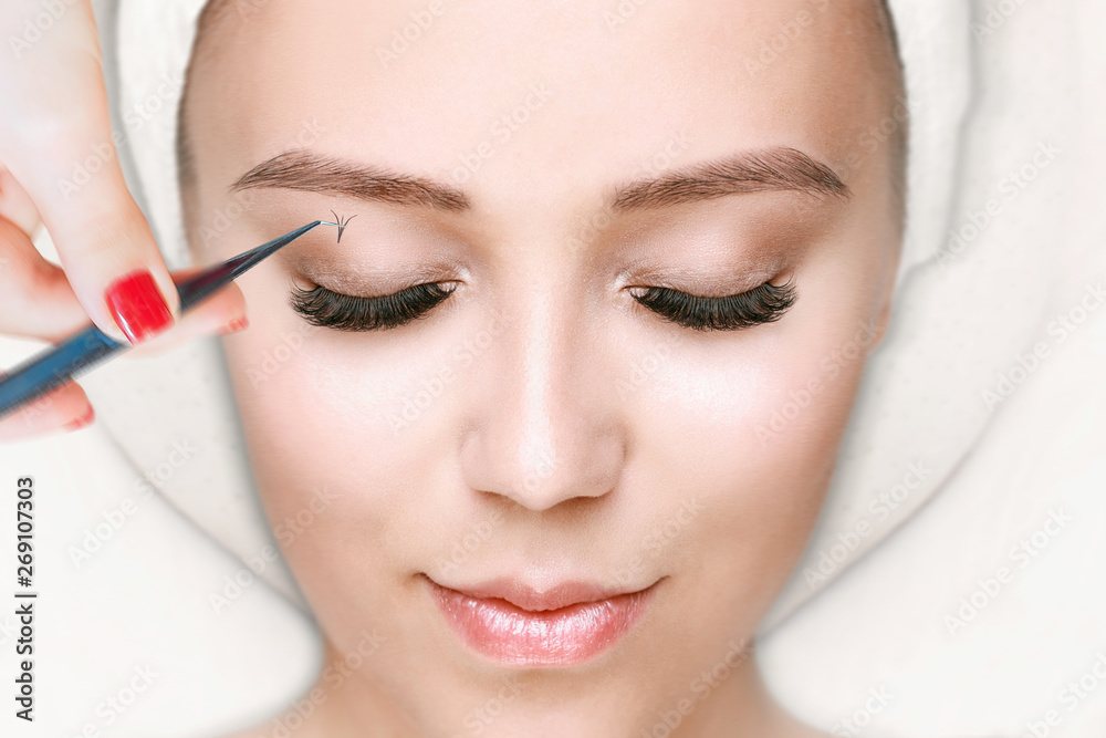 Eyelash Extension Procedure. Close up view of female eyes with long eyelashes. Stylist holding tweezers, tongs and making lengthening lashes. Macro, selective focus.