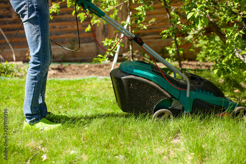 Young man mowing the lawn. Worker doing his job in backyard. Spending summer day in garden. Lawnmower standing on the background of private garden.
