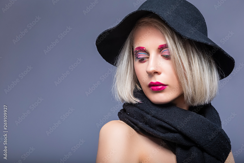 Portrait of Beautiful Caucasian Blond Girl in Black Hat Over Gray Background with Facial Make-Up. Portrait of Beautiful Caucasian Blond Girl in Black Hat Over Gray Background with Facial Make-Up.
