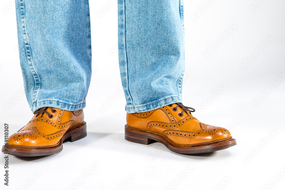 Closeup of Mens Legs on Brown Oxford Brogue Shoes. Posing in Blue Jeans Against White Background.