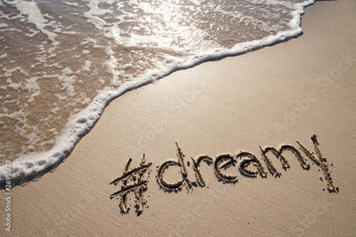 Modern dreamy message for the beach with a social media-friendly hashtag written in smooth sand with incoming wave