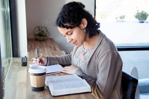 black woman studies her bible while drinking coffee and making notes