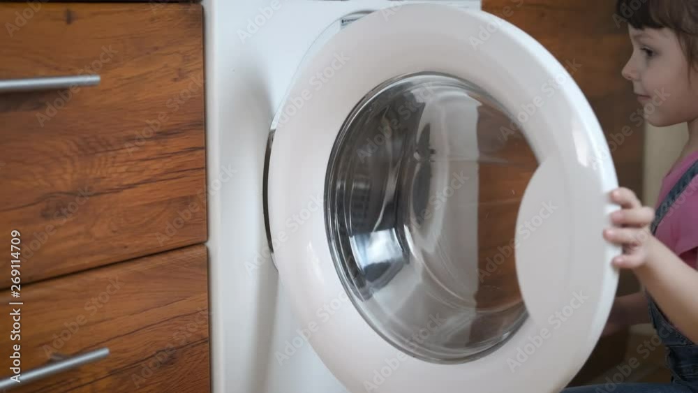 The child gets into the washing machine. Happy little girl climbs into the washing machine. The child gets into the washing machine. Happy little girl climbs into the washing machine.
