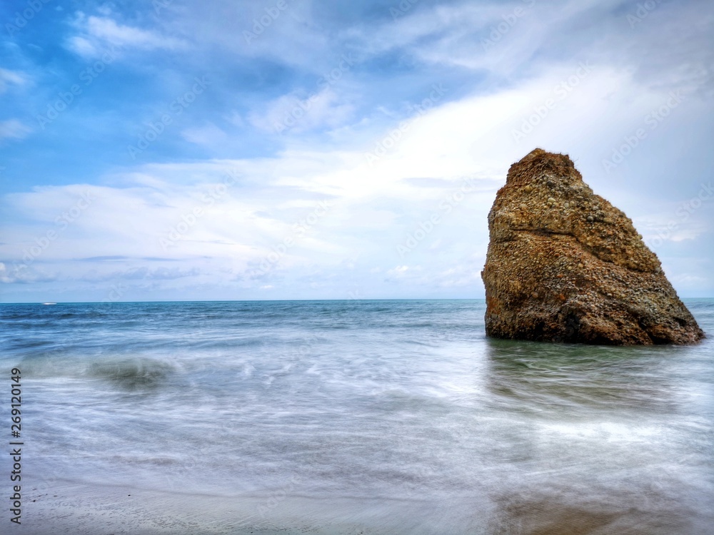 Beautiful single rock formation on the seashore with splashing swash  silky smooth water reflection background.