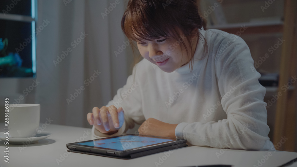 Young asian woman working late using tablet checking social media while relax on desk in night in living room at home. Enjoying time at home concept. Young asian woman working late using tablet checking social media while relax on desk in night in living room at home. Enjoying time at home concept.
