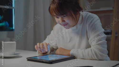 Young asian woman working late using tablet checking social media while relax on desk in night in living room at home. Enjoying time at home concept.