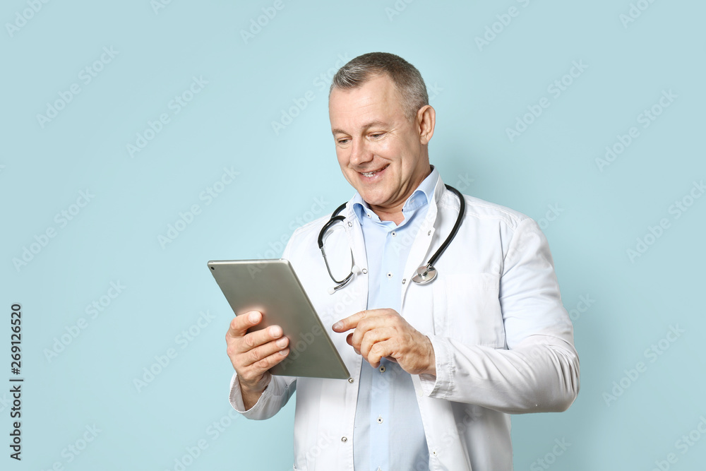Handsome middle-aged doctor with tablet PC on color background Handsome middle-aged doctor with tablet PC on color background