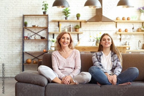 Happy mother and daughter sitting on sofa at home