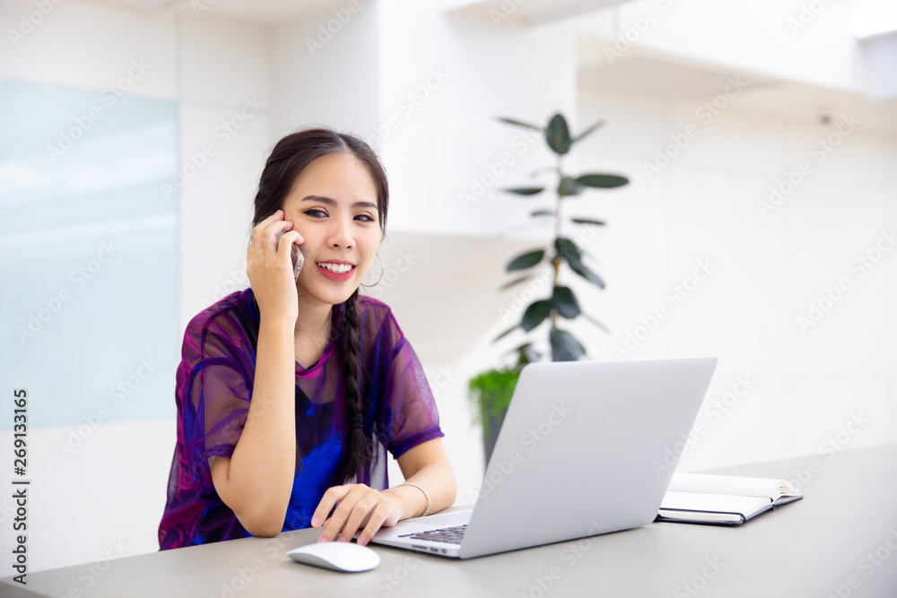 Young business female using smart phone while working on computer laptop in modern office. Young business female using smart phone while working on computer laptop in modern office.