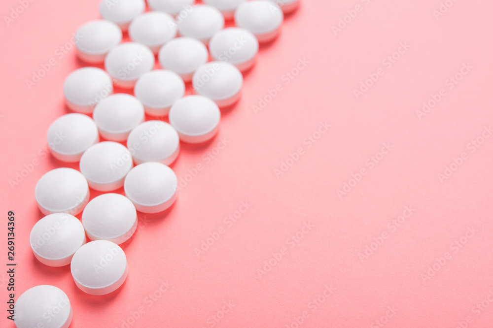 Closeup of white pills on a pastel pink color background Closeup of white pills on a pastel pink color background