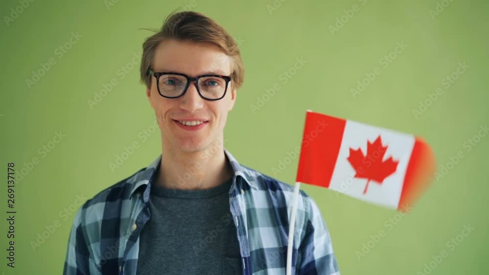 Slow motion portrait of handsome guy in trendy glasses Canadian citizen holding national flag of Canada smiling looking at camera on light green background. Slow motion portrait of handsome guy in trendy glasses Canadian citizen holding national flag of Canada smiling looking at camera on light green background.
