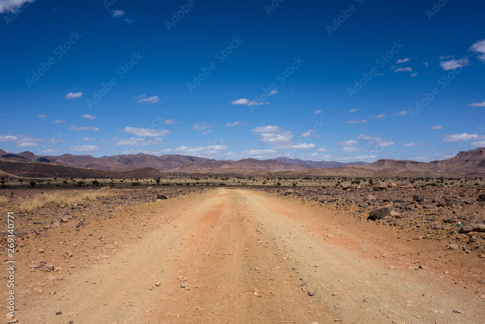 Dirt road with some rocky desert landscape on a road-trip from Marrakesh to Merzouga, Morocco Dirt road with some rocky desert landscape on a road-trip from Marrakesh to Merzouga, Morocco