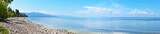 Panoramic view of Baikal Lake on a sunny summer day. Pebble beach and coastal grove. In the distance, tourists are resting. Beautiful water landscape
