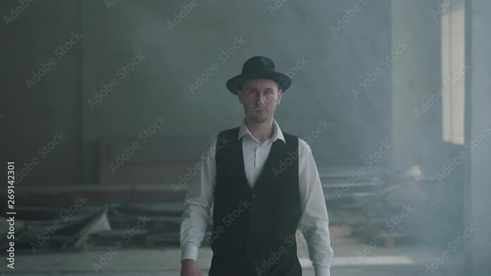 Portrait handsome confident man in a hat walking to the camera holding a gun in an abandoned building. The head of the mafia is in an empty building. Cool guy, thug, mafia. Slow motion. Portrait handsome confident man in a hat walking to the camera holding a gun in an abandoned building. The head of the mafia is in an empty building. Cool guy, thug, mafia. Slow motion.