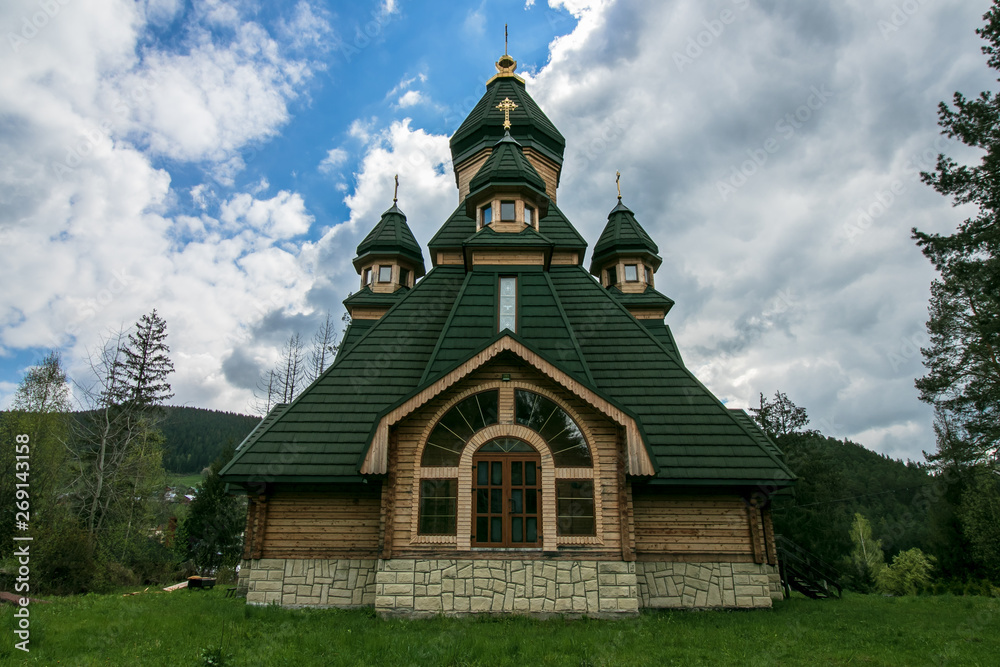 Wooden green chapel on a hill in the forest. Rustic chapel. Church against the forest and sky. Orthodox, christian monastery in summer.