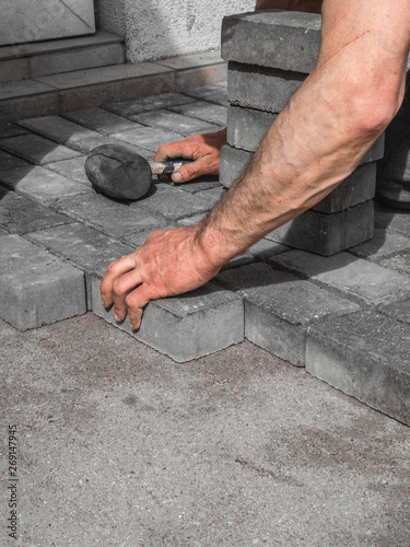 Hands of a manual worker laying concrete paving blocks.