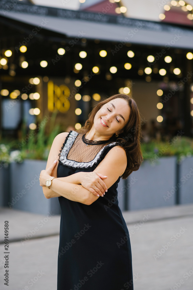 Fototapeta premium A woman with dark hair, middle-aged, closed her eyes and smiles, hugging herself with her hands. The concept of peace, happiness and tranquility in the soul