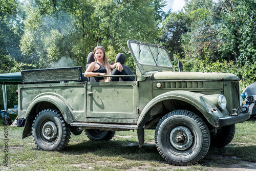 Woman outdoors sitting on hood of military car