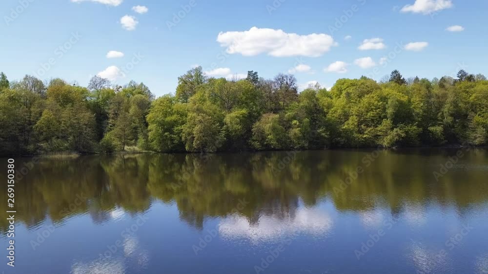 Aerial. Small lake surrounded by green trees. Shot from a low flying drone. Slow, cinematic dolly shot right. Spring 2019. Aerial. Small lake surrounded by green trees. Shot from a low flying drone. Slow, cinematic dolly shot right. Spring 2019.