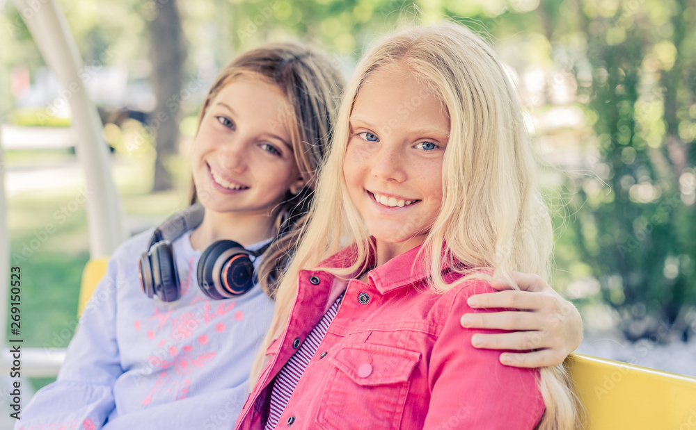 Fototapeta premium Pretty smiling teenage girls sit hugging together on the bench