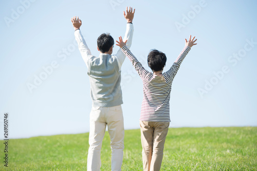 草原で両手を挙げるシニア夫婦の後姿