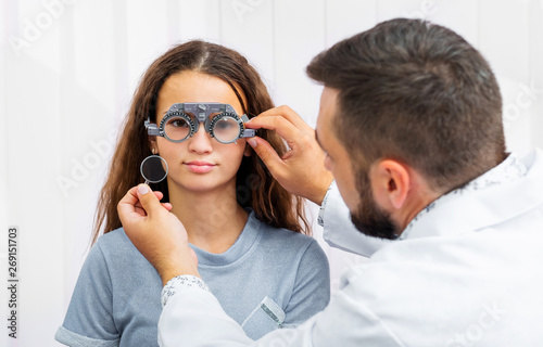 Doctor holding special eye equipment examinating girl's eyes in the ophthalmologic clinic