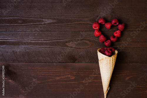 Fresh organic homemade garden raspberries in a waffle ice cream cone and a raspberry heart on a brown board background. The concept of natural nutrition, ice cream. Copy left view © Sunshine