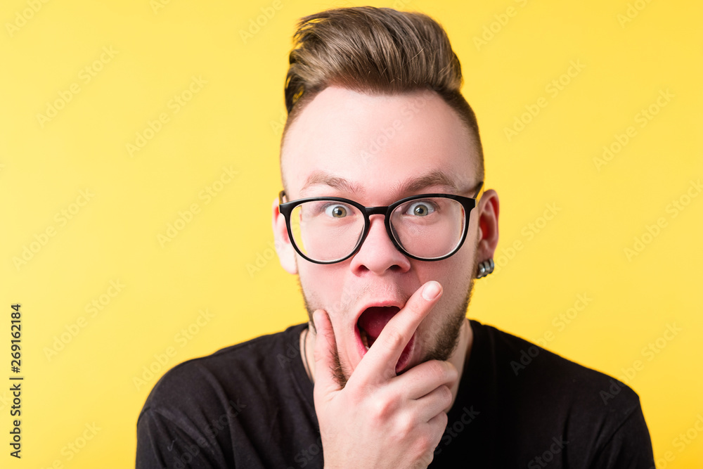 Portrait of amazed hipster guy on yellow background. Young emotional man in glasses. Shocked facial expression. Copy space. Portrait of amazed hipster guy on yellow background. Young emotional man in glasses. Shocked facial expression. Copy space.