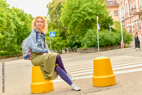 young attractive curly blonde woman sitting on a concrete fence near the pedestrian crossing