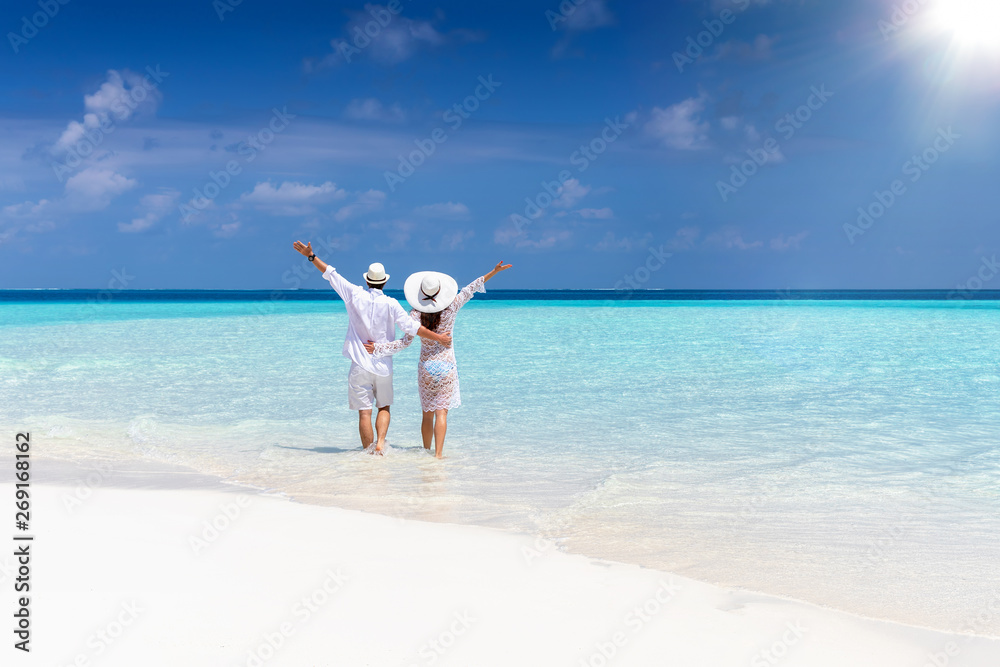 Glückliches Paar in weißen Sommerkleidern spaziert am tropischen Strand und genießt den Urlaub Glückliches Paar in weißen Sommerkleidern spaziert am tropischen Strand und genießt den Urlaub