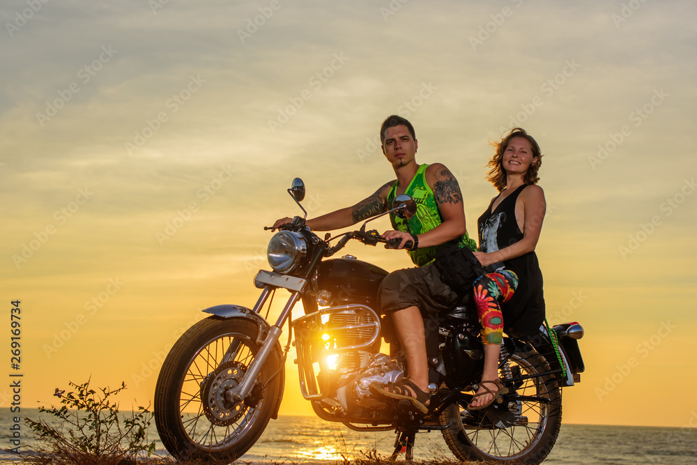 Fototapeta premium Romantic picture with a couple of beautiful stylish bikers at sunset. Handsome guy with tatoo and young sexy woman enjoy themselves in motorbike trip.