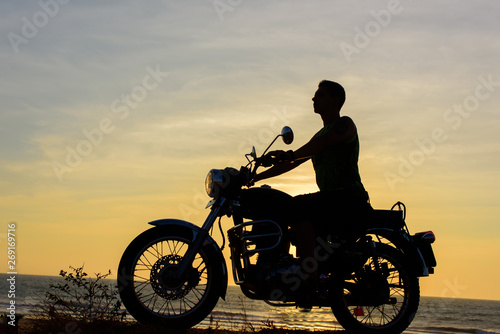 Silhouette of guy on motorcycle on sunset background. Young biker are sitting on motorcycle, face in profile. Moto trip on the seaside, freedom and active lifestyle. © exebiche