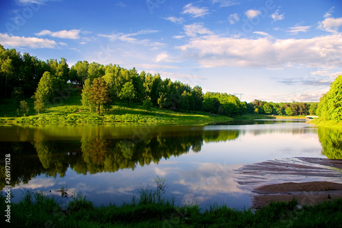 Reflection of the sky in the blue of a calm lake. Forest, illuminated by the sun, on the opposite Bank. Russia