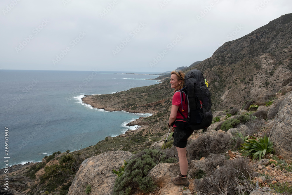 A woman with a backpack is hiking along the coastline on the greek island Crete