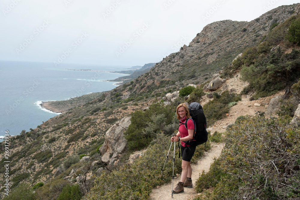 A woman with a backpack is hiking along the coastline on the greek island Crete