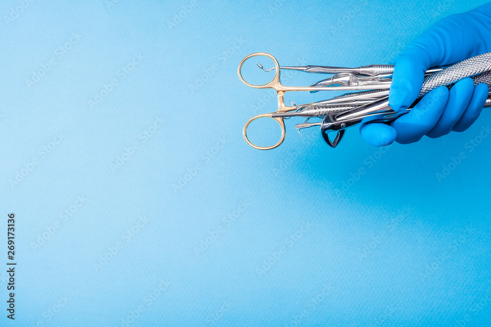 Fototapeta premium Hand in blue glove holding surgery dental tools on light blue background