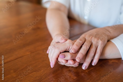 Elderly mother and her daughter holding hands while sitting at the table.Close up on women of different generations holding hands. Close Up Shot Of Mother And Daughter's Hands Holding