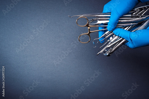 Hands in blue gloves holding metal dental equipment on gray background with copy space photo