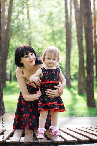 Happy mother and lovely little daughter are sit on bench under trees shades at sunny spring park. Childhood lifestyle. Concept of a happy family. Mother and kid. Universal Children's Day