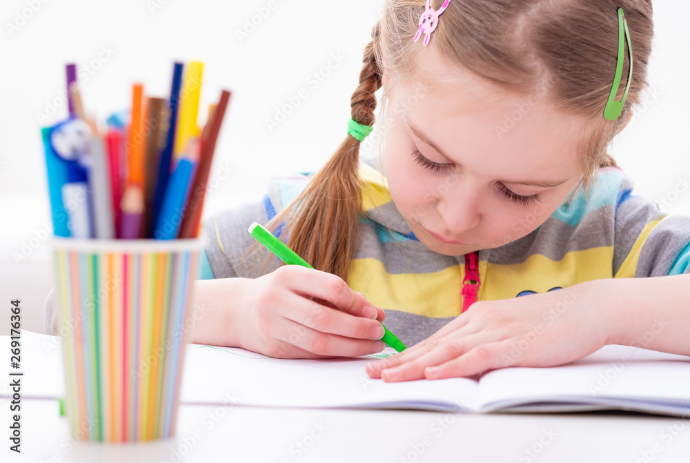 Adorable young female pupil carefully working in her copybook, on white background Adorable young female pupil carefully working in her copybook, on white background