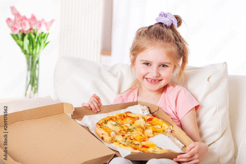 Smiling little girl eating pizza, on the couch