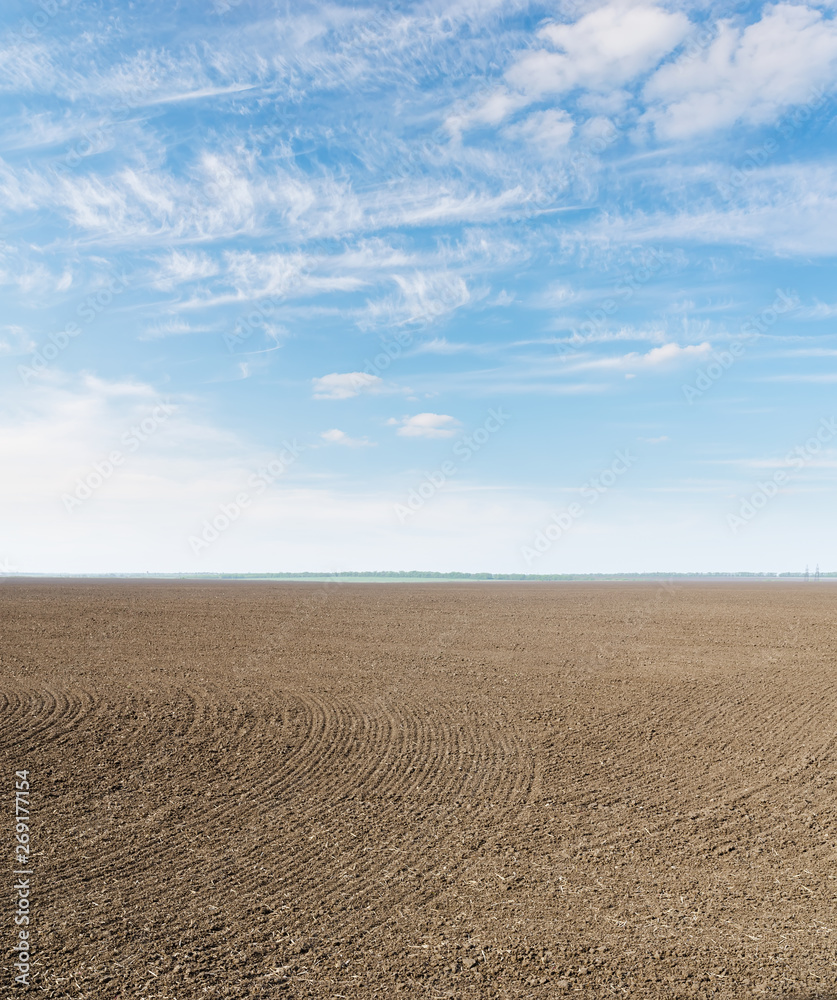 black plowed field and clouds in blue sky black plowed field and clouds in blue sky