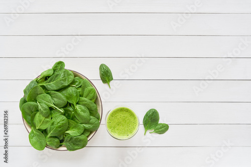 Green smoothie from spinach in glass jar and plate with fresh spinach on white wooden background. Copy space.