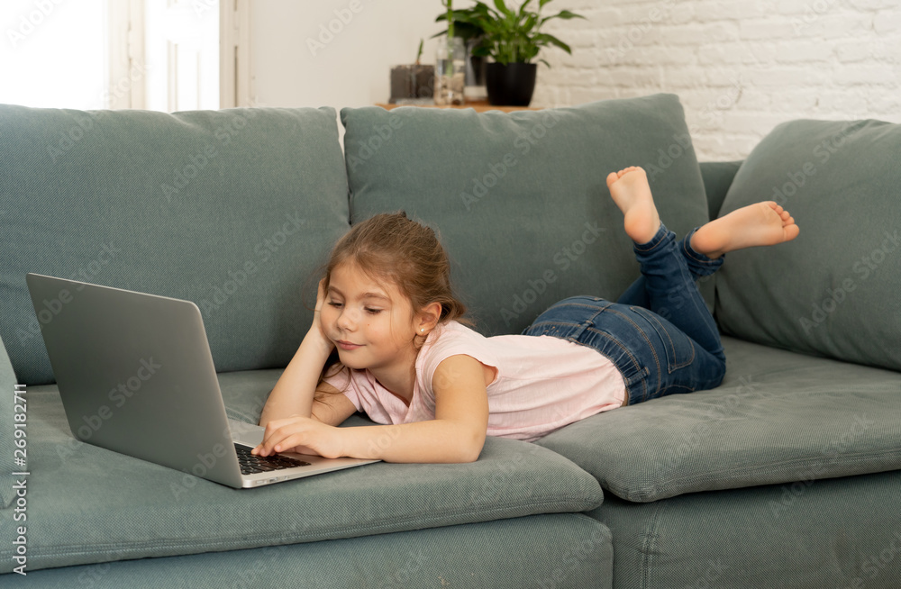 Beautiful cute charming little girl playing and surfing the internet on laptop smiling at home Beautiful cute charming little girl playing and surfing the internet on laptop smiling at home