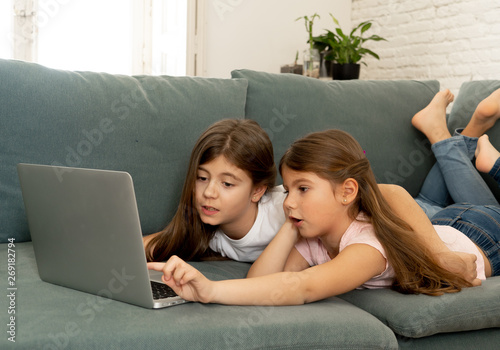 Two sisters smiling and having fun together playing and surfing on the internet on a laptop