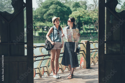 Canvas Print two asian women tourists with paper map standing outside wood japanese style temple searching right way information
