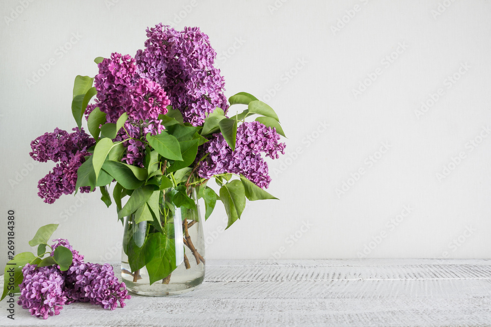 Bouquet of purple lilac flowers in glass vase in white interior. Space for text. Bouquet of purple lilac flowers in glass vase in white interior. Space for text.
