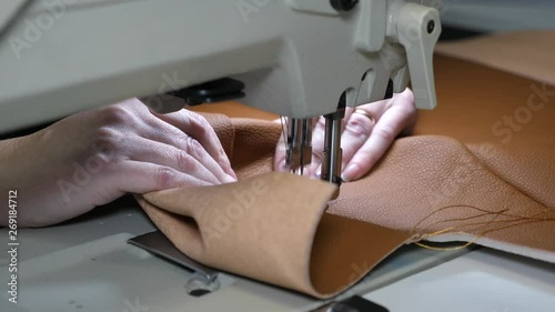 tailor sews brown leather in sewing workshop. two needles of sewing machine quickly moves up and down, close-up. rocess of sewing artificial leather. needle of sewing machine in motion. photo