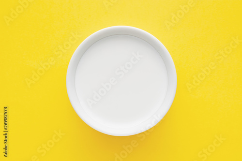 Valokuva Milk in a white bowl on yellow background. Close up top down view